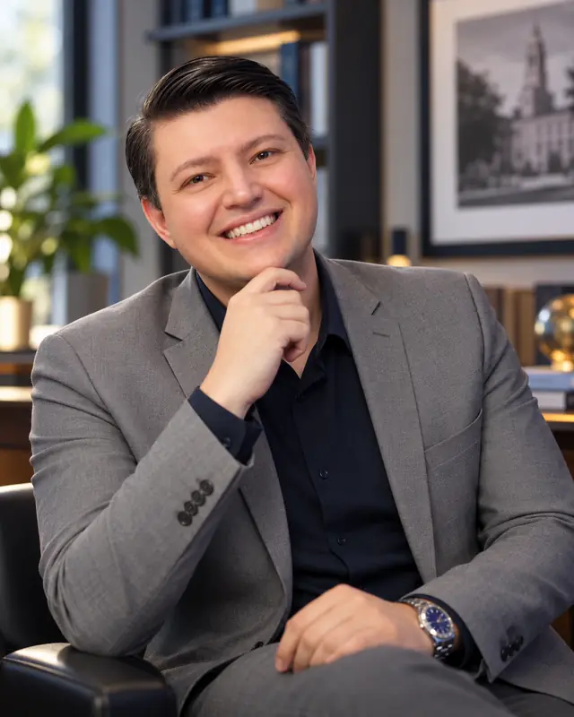 Marcos Costa, professor universitário, sorrindo, de paletó cinza, em uma biblioteca